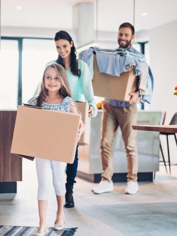 a little girl holding a box while standing with her family in the kitchen