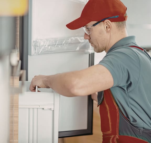 A man in a red cap and overalls is installing a white radiator.