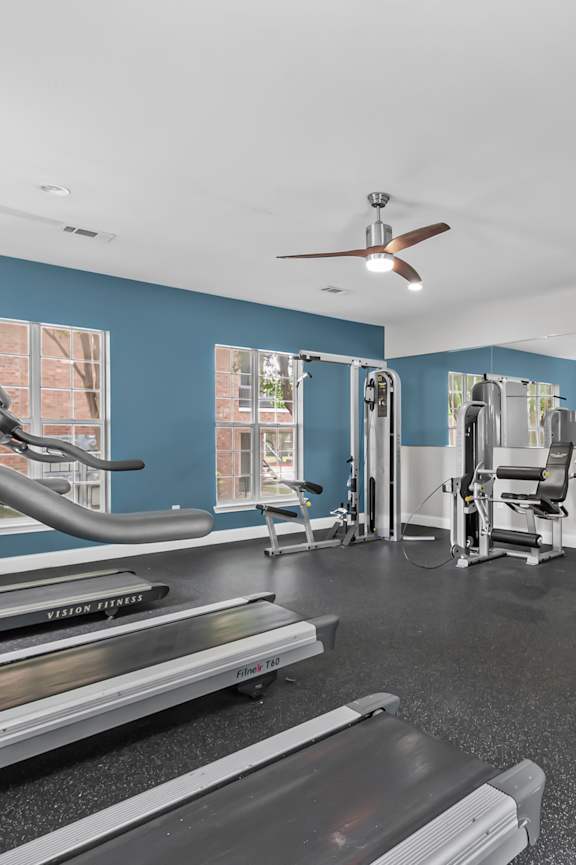 A spacious gym with treadmills, elliptical machines, and a fan.