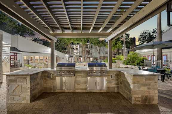A stone barbecue area with a grill and a table is under a roof.