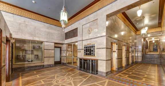 A large, empty lobby with a marble floor and a chandelier hanging from the ceiling.
