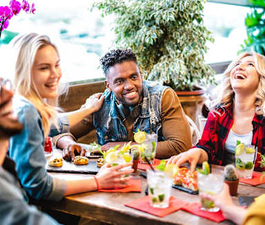 A group of people are sitting around a table, laughing and enjoying drinks and food.
