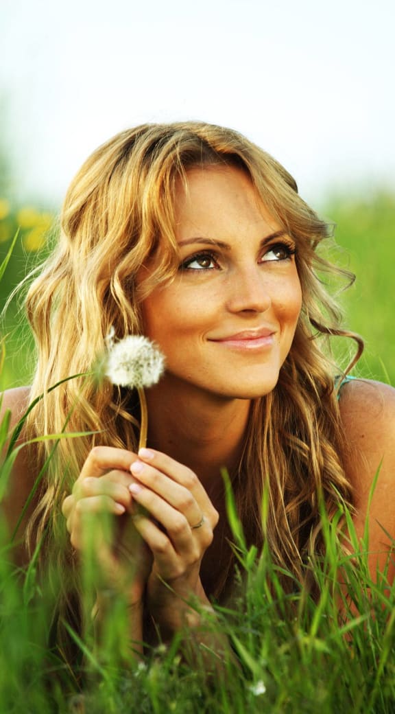 a woman laying in the grass holding a dandelion