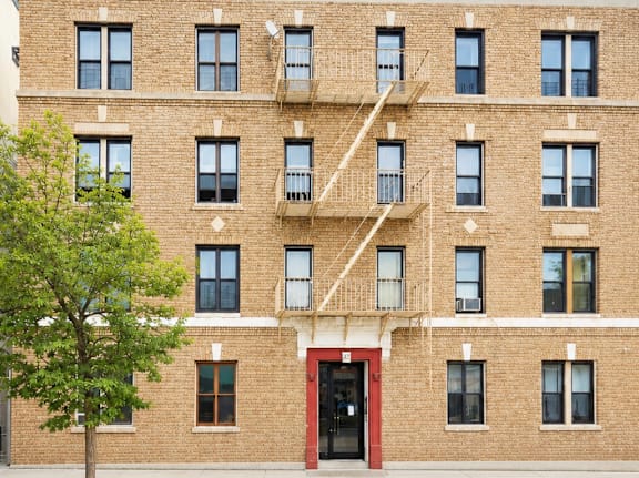 A red door is on the ground floor of a brick building.