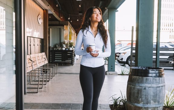 a woman walking down a sidewalk with a cup of coffee in her hand