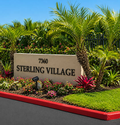 A sign that says Sterling Village in front of some plants.