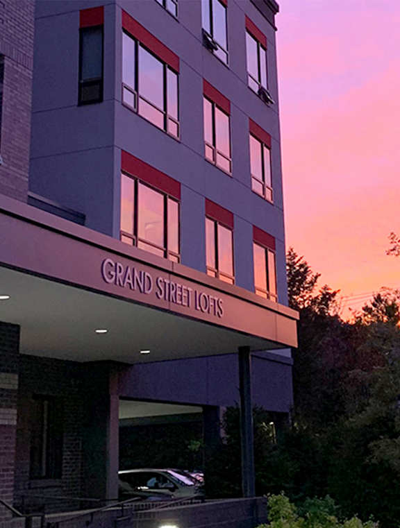 A modern building with a grey and red facade is labeled Grand Street.