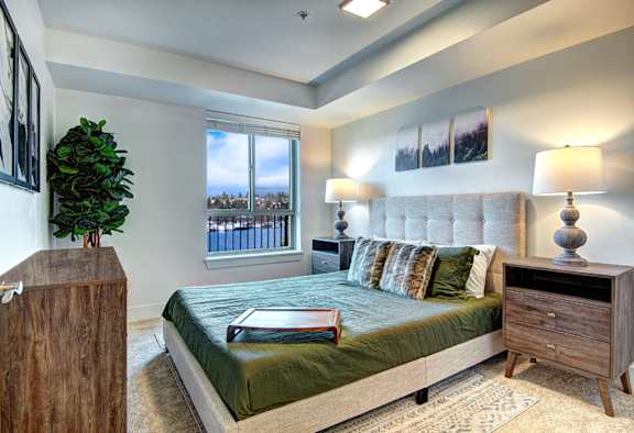 A bedroom with a large bed, a wooden dresser, and a window overlooking a cityscape.