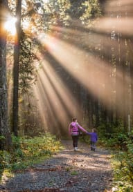 a woman and a child walking down a path in the woods