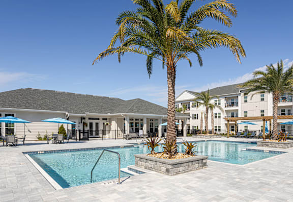 A large swimming pool in front of a building with palm trees.