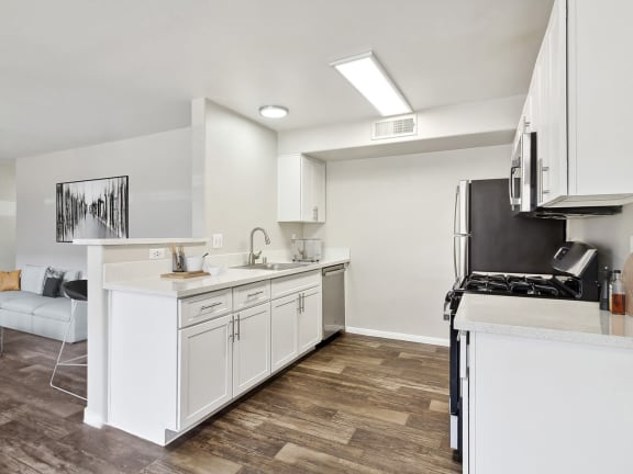 Model Kitchen with Wood-Style Flooring, White Cabinets and View of Living Room at Loma Vista Apartments in Las Vegas, NV-LRGAM.