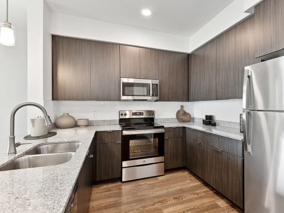 Model Kitchen with Dark Wood Cabinets and Wood-Style Flooring at Parc Roundtree Ranch Apartments located in Peoria, AZ-LRGAM.