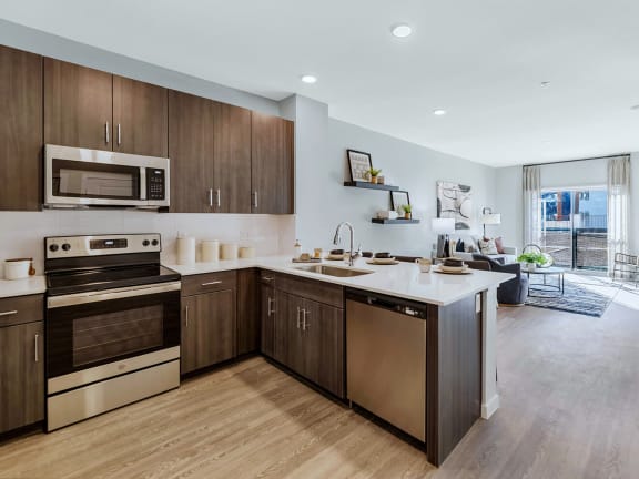 Model Kitchen with Dark Wood Cabinets, Wood-Style Flooring and View of Living Room at Glen 91 Apartments located in Glendale, AZ-LRGAM.