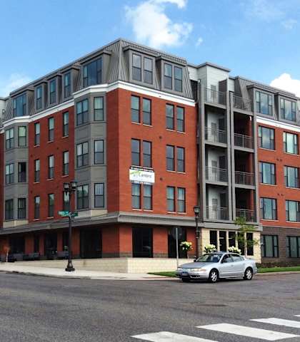an apartment building on a street corner with cars parked in front of it at The Cambric Senior Apartments, St. Paul