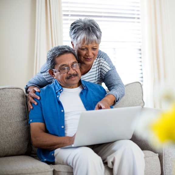 A woman is helping an older man with his laptop.