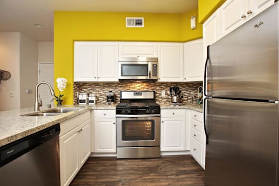 A kitchen with a yellow wall and stainless steel appliances at The Kitt at Warner Center in CA, 91303