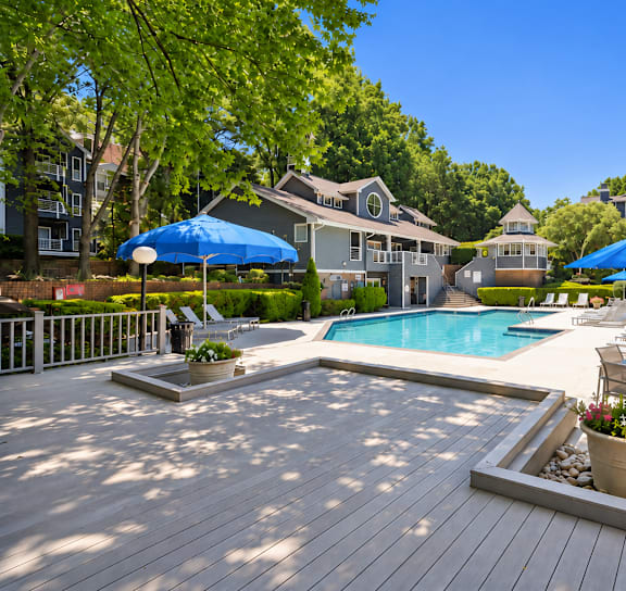 A pool surrounded by a deck with a few chairs and umbrellas.