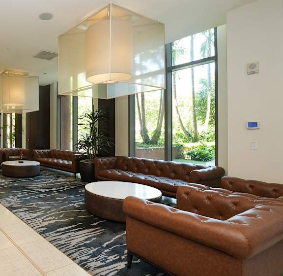 A long brown couch is in the middle of a room with a round table and a lamp.