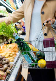 a woman in a grocery store with a shopping basket and a bottle of wine
