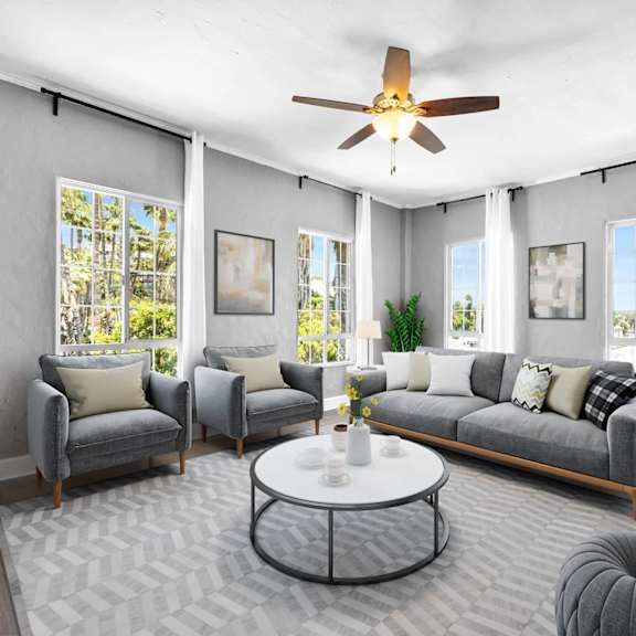 A living room with a grey sofa, two grey armchairs, a white coffee table, and a ceiling fan.