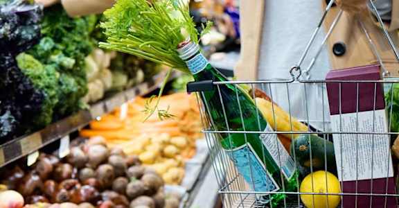 a woman in a grocery store with a shopping basket and a bottle of wine