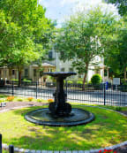 a fountain in the middle of a grassy area with trees in the background
