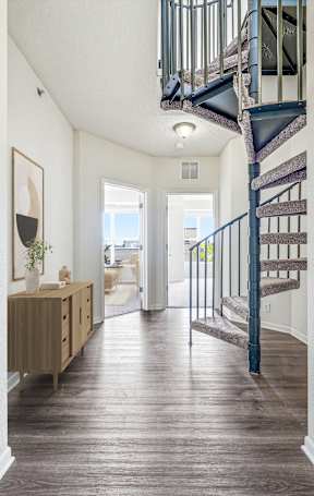 A hallway with a staircase and a cabinet with a vase on it.