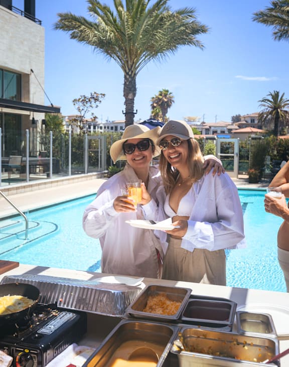 Two people are standing by a pool with food trays in front of them.