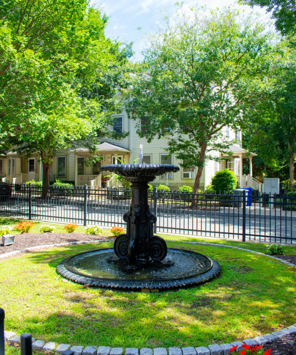 a fountain in the middle of a grassy area with trees in the background