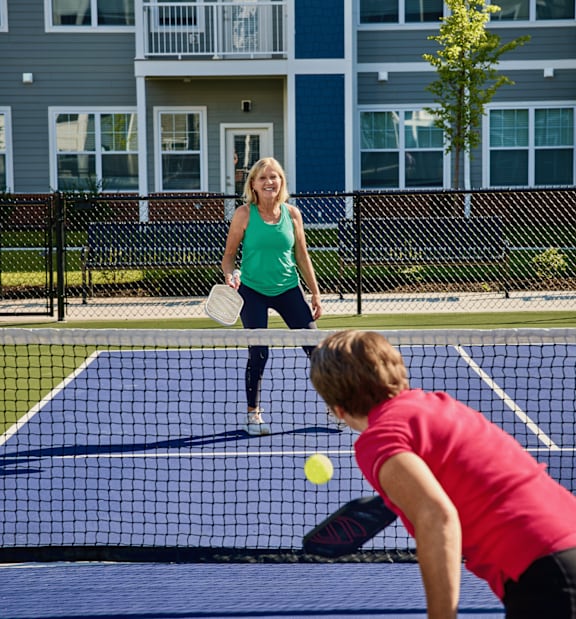 A woman in a green top and a man in a red top playing tennis on a blue court.