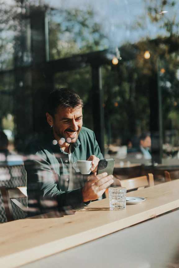 A man in a green shirt is sitting at a table with a cup of coffee and a glass of water.