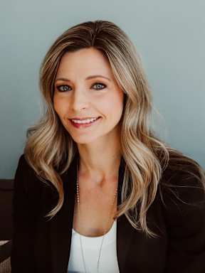 A woman with blonde hair wearing a black blazer and a white top with a necklace.
