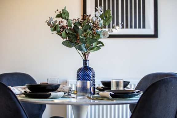 A blue vase with flowers sits on a table with plates and glasses.