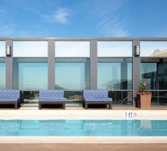 a row of blue chairs sit in front of a glass walled building with a swimming pool