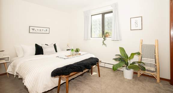 A bedroom with a bed, chair, and potted plant.