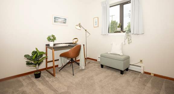 A room with a desk, chair, and potted plant.