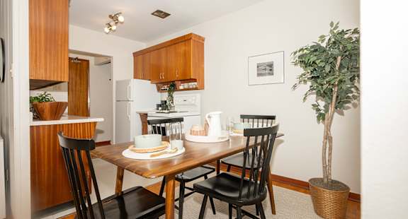 A dining room with a table set for two and a potted plant.