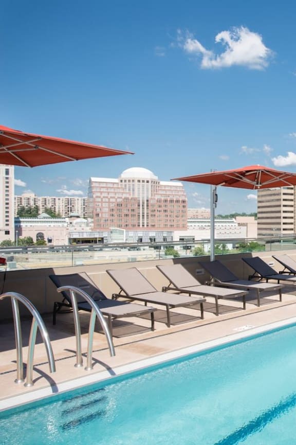 a swimming pool with lounge chairs and umbrellas next to a tall building
