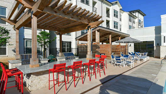 a patio with red chairs and a table with chairs at The Eddy at Riverview, Smyrna, 30126