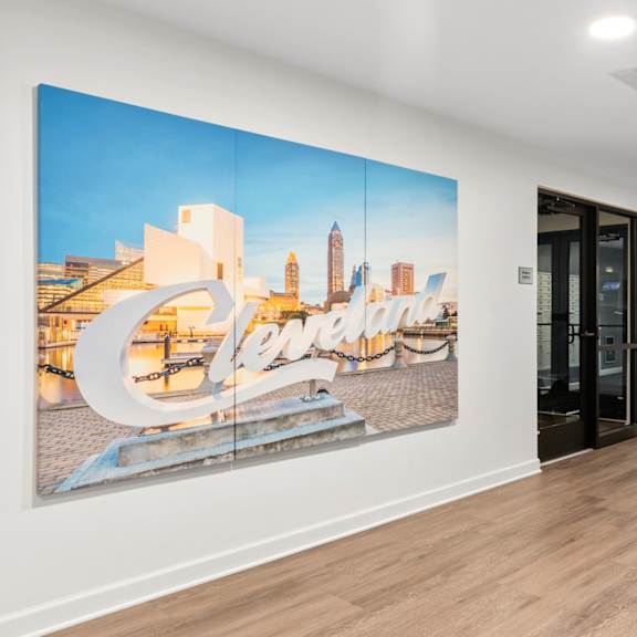 A large picture of a cityscape with the word "Cleveland" written on it is hanging on the wall of a room with wooden floors and black doors.