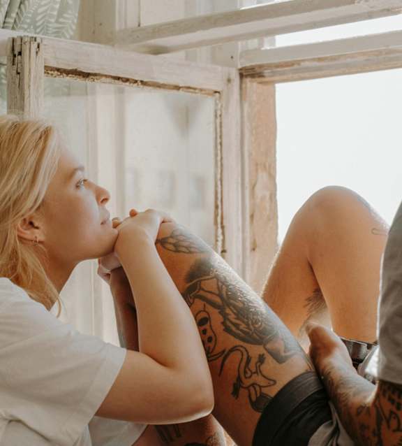 A woman with a tattooed arm is sitting next to a man with a tattooed leg.