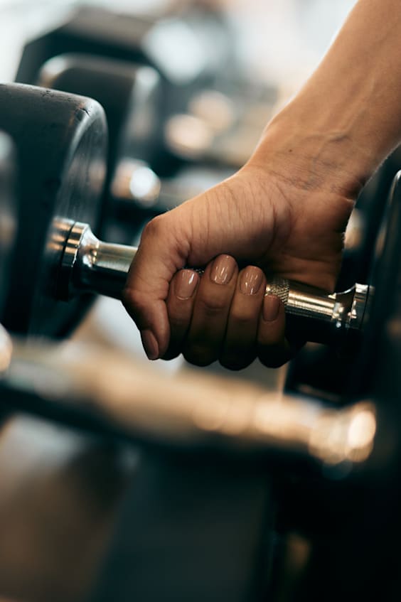 A person's hand is gripping a dumbbell in a gym setting.