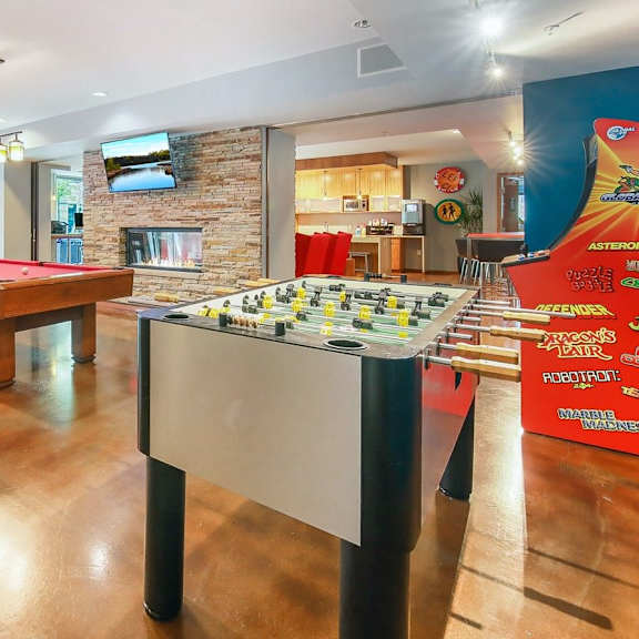 Lounge with games such as foosball, pool, and arcade games, as well as tables, chairs, and a community kitchen at Blue and Lime Apartments. 