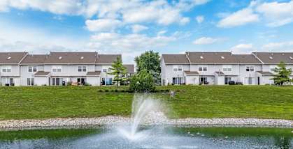 A fountain in the middle of a pond with houses in the background.