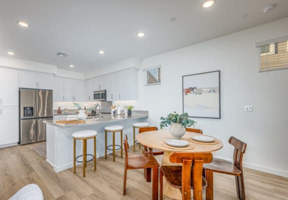 A kitchen with a table and chairs in the foreground and a fridge and microwave in the background.