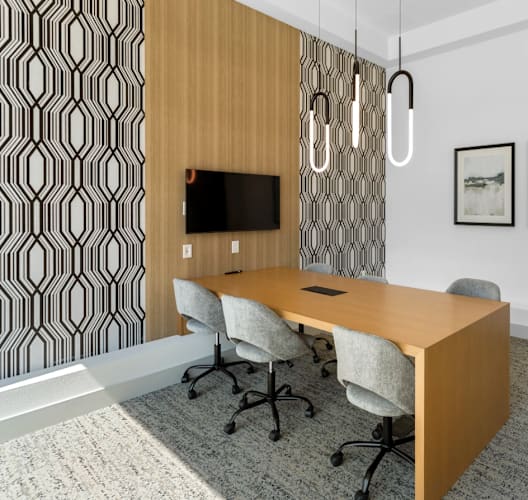 A conference room with a wooden table and chairs, a television, and two framed pictures on the wall.