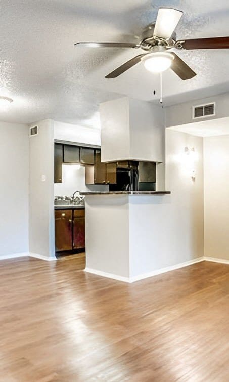 an empty living room with a ceiling fan and a kitchen