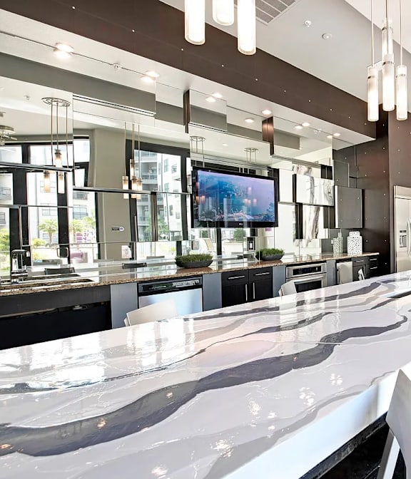 A long white marble bar with white chairs and a TV on the wall.