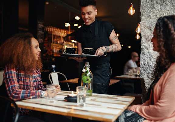A waiter is serving food to two women at a restaurant.