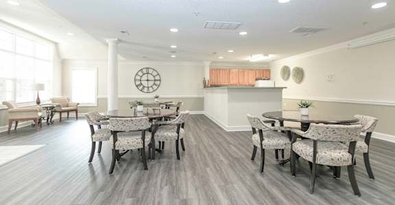 a room with a table and chairs and a kitchen in the background